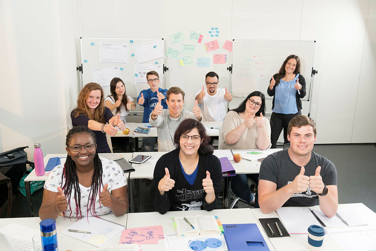 Schulklasse im Unterricht zeigt Daumen nach oben mit Whiteboards und Unterrichtsmaterial.